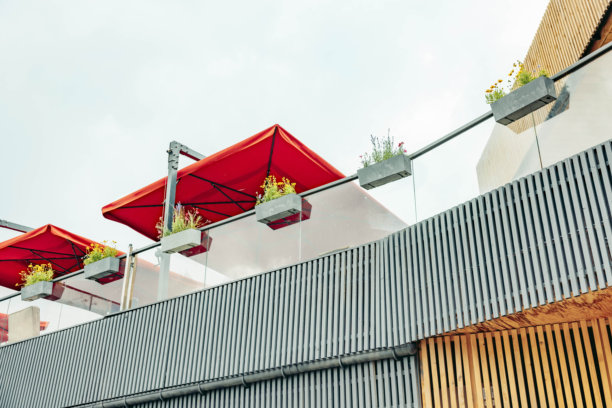 现代建筑，拥有木质外墙和金属点缀。红色雨伞和绿色植物装饰着屋顶露台。整个场景暗示着山区的一个休闲空间。图片下载