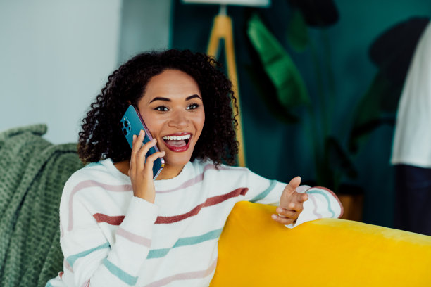 年轻女子在家中愉快地使用手机，坐在色彩鲜艳的客厅里明亮的沙发上，生活方式社交媒体图库照片图片下载