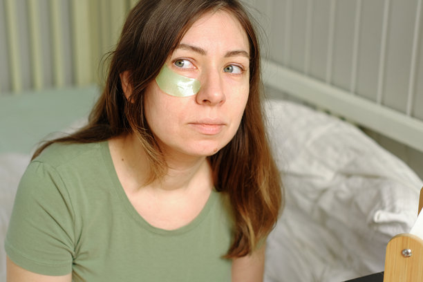 一位40多岁的女性正在早晨进行面部自我护理，她用滴管将精华液涂抹在脸上，进行皮肤护理。女性用油性滴管涂抹精油，用于化妆品广告和健康。图片下载