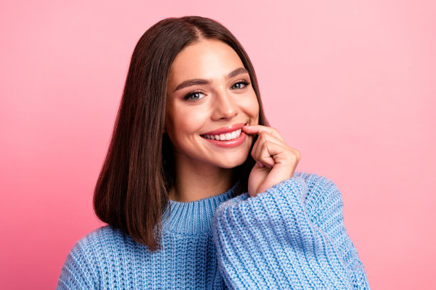 一位年轻的棕色头发女性，身穿蓝色针织毛衣，在粉色背景前摆姿势，用于生活时尚风格的图片。图片下载