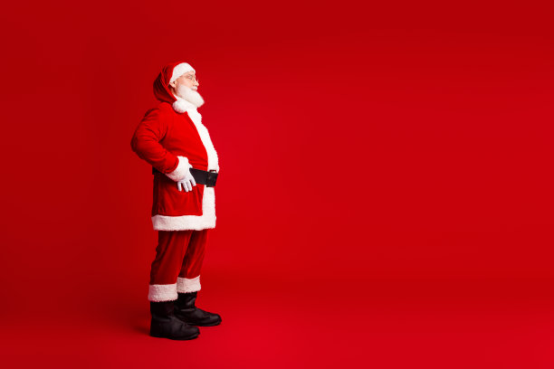 身穿红色服装、留着白色胡子的圣诞老人站在影棚内，背景是纯红色，适合节日季的素材照片图片下载