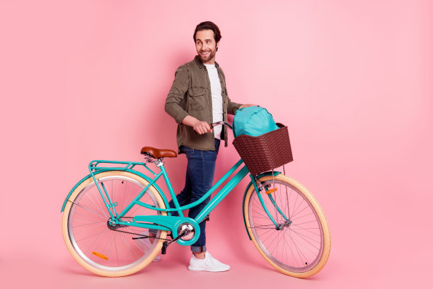 年轻男子的全身侧面照片，带着快乐积极的微笑，看向空白空间，背景是粉彩色，适合自行车旅行，独立拍摄图片下载