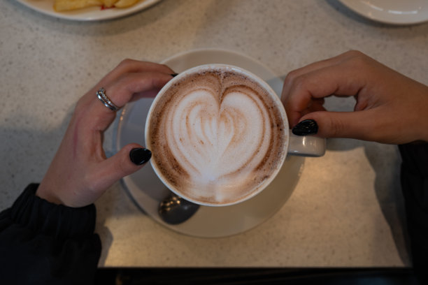 双手捧着一杯带有心形拉花咖啡的杯子图片下载