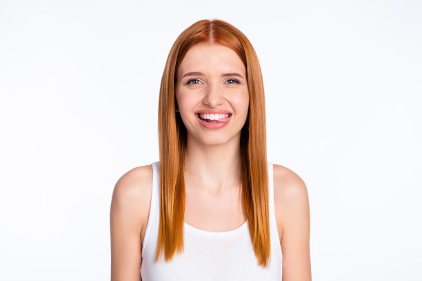 身穿白色上衣、扎着红色头发的女士伸出舌头，露出开心的表情，背景是明亮的彩色。此照片为室内拍摄。图片下载