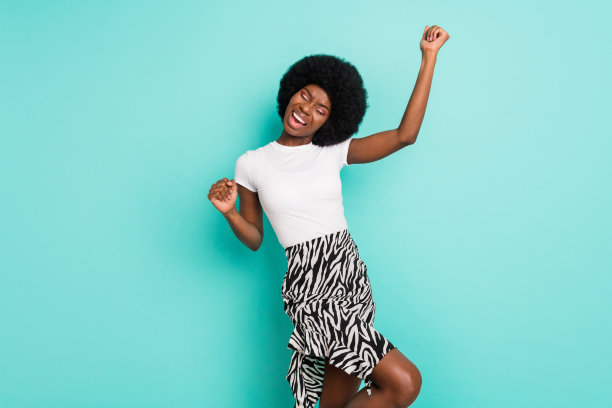 照片：一位可爱的幸运的深肤色女性，穿着休闲装，面带微笑，举起拳头，背景是孤立的绿松石色图片下载