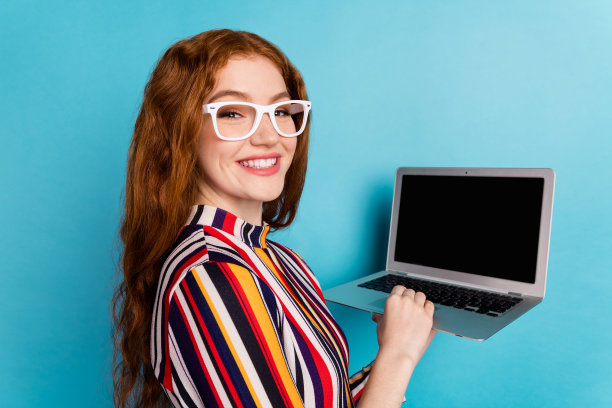 一位戴着眼镜、穿着彩色衬衫的红发女士的个人资料照片，她正使用笔记本电脑工作，背景为蓝色，表情滑稽图片下载