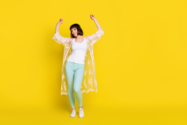 快乐活泼的年轻女子，心情愉悦，举起双手跳舞，在黄色背景下拍摄的全身照片图片下载
