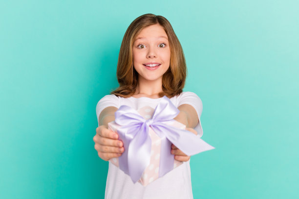 照片肖像：快乐的女学生在生日派对上赠送礼物盒，背景为鲜艳的绿松石色。图片下载