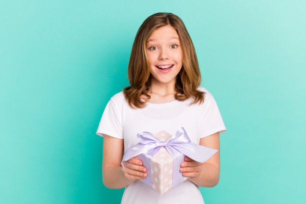 照片肖像：快乐的小学女生，手持礼物盒，背景为鲜艳的绿松石色图片下载