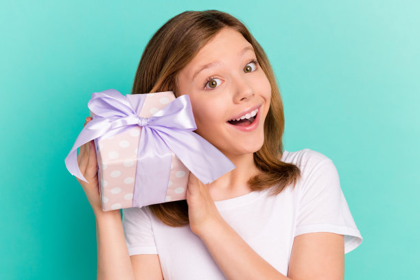 照片肖像，快乐的女学生拿着礼物盒子，猜测里面是什么，背景是鲜艳的绿松石色图片下载