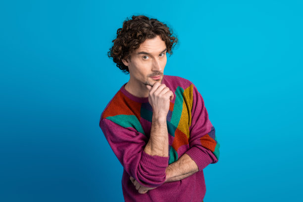 身穿彩色毛衣的思考男子在蓝色背景前摆姿势，用于时尚生活方式的素材照片图片下载