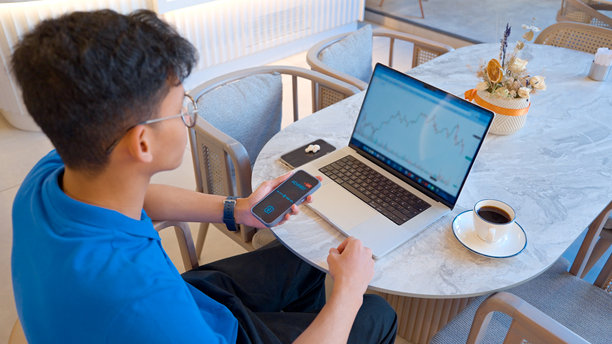 年轻男子在咖啡馆使用笔记本电脑上的AI工具分析股票市场数据图片下载