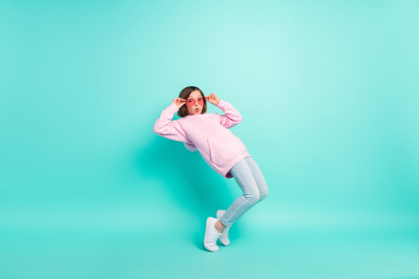 粉色眼镜运动服的棕发小女孩，身穿运动服，在蓝绿色背景前跳舞，个人资料全尺寸照片图片下载