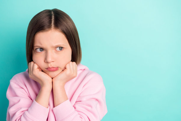 照片：短发悲伤小女孩，双手捂脸，眼神空洞，身穿粉色运动服，背景为蓝绿色图片下载