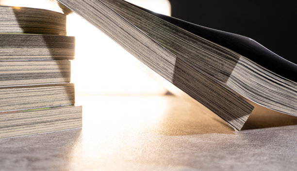 从后面明亮照明的书本堆叠的特写水平视图，展示了磨损的书页边缘和柔和的对比度，适合教育或复古阅读视觉。图片下载