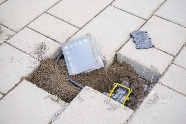 铺设地砖的嵌入式发光块安装。用于户外路径或广场的地下照明系统，包含电缆和外壳。适用于工程、城市修复、基础设施项目。实景照片。图片下载