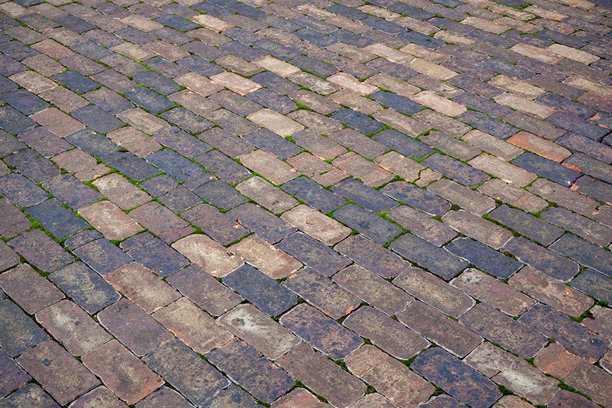 旧鹅卵石铺砌路面，砖缝间长有苔藓。对角线图案的表面，适用于历史街道、庭院或花园小径。真实照片图片下载