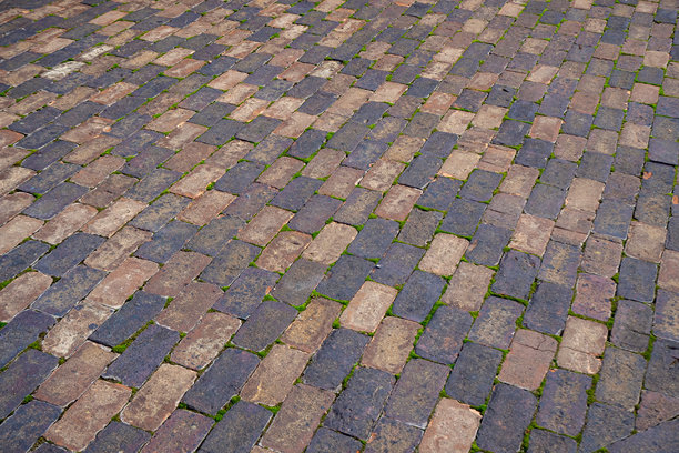 长满苔藓的旧鹅卵石路面，石头缝隙间有风化的砖块。真实照片。图片下载