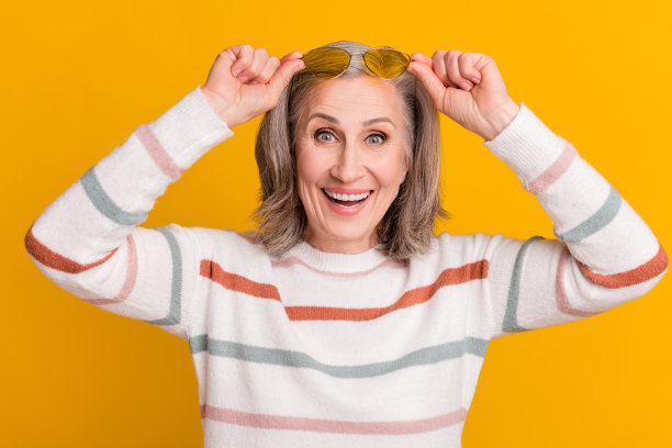 身穿白色毛衣、戴着眼镜、面带微笑的时尚时髦退休女士，在黄色背景前的照片图片下载