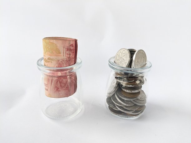 照片展示了两个放在白色背景上的小型透明玻璃容器。左边的容器里装着一张整齐卷起的纸币。图片下载