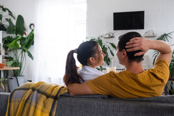 一男一女在家中白色内饰的沙发上观看电视，电视屏幕为黑色模拟画面。居家休闲、娱乐、爱情、家庭、约会图片下载