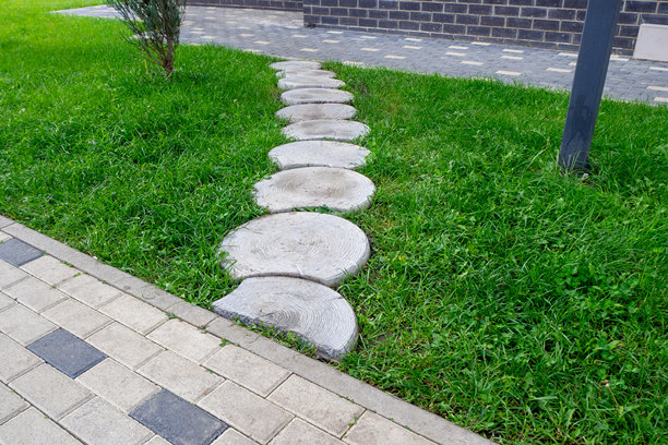 花园小径由圆形混凝土踏步石铺成，位于绿色草坪旁的人行道旁边，是清晰的园林景观元素。可用于园林绿化、花园设计、建筑、城市规划。真实照片。图片下载