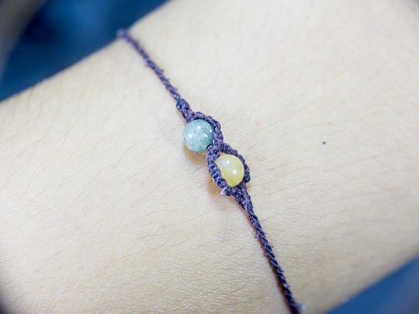 特写手腕上手工编织的流苏手链，配有两颗绿色和黄色的小珠子。图片下载