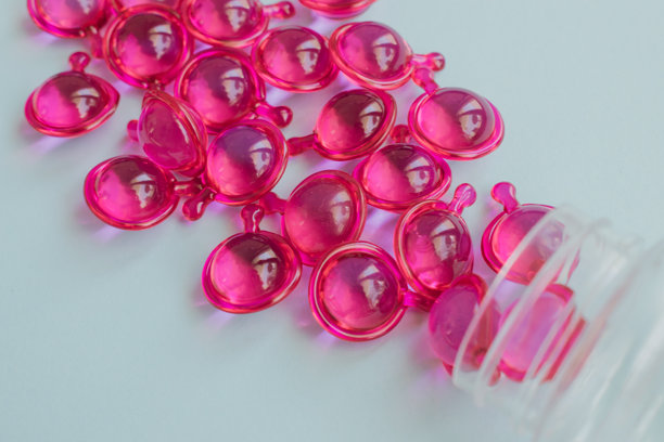 从塑料瓶中溢出的鲜艳粉色护发精华胶囊，适用于干枯、受损和毛躁发质。浅蓝色背景特写。图片下载
