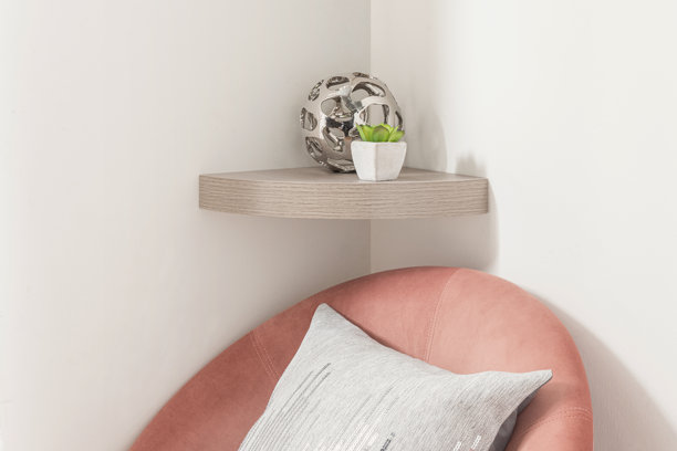 一款时尚室内角落的细节照片，特色是弧形浅木色角落置物架，上面摆放着一件金属抽象雕塑和一小盆多肉植物。图片下载