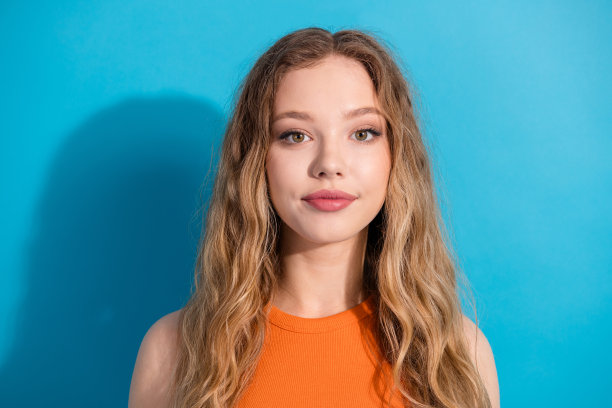 身穿橙色上衣的年轻金发女郎在蓝色背景前摆姿势，适合时尚生活方式的素材摄影图片下载