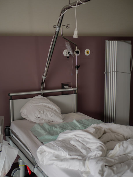 现代医院病床，配有白色枕头、褶皱的毯子和输液架，位于宁静的病房内。高质量照片图片下载