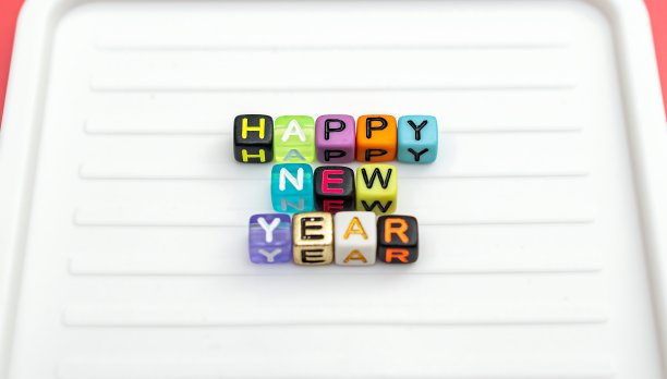 色彩缤纷的珠子在白色字母板上拼出“新年快乐”的字样。图片下载