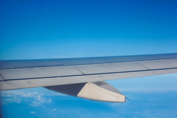 这张图片展示了从飞机窗外看到的景象，可以看到部分飞机机翼，以及翼尖小翼。天空晴朗，下方有一层云，表明飞机正在飞行中。图片下载