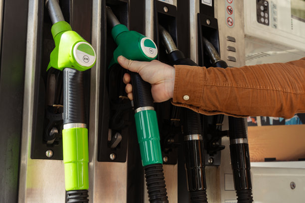 加油站加油时，一只手拿着油枪，旁边是色彩鲜艳的油泵图片下载