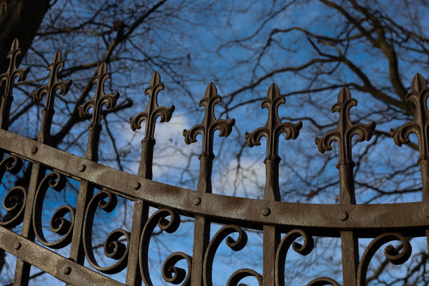 这张照片展示了一个复古锻铁门或栅栏的上半部分特写，装饰性的十字形顶饰在深蓝色天空的映衬下显得格外醒目。图片下载