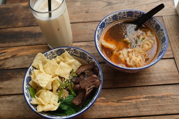 一顿丰盛的亚洲餐，包括一碗干面配烤牛肉和饼干、一碗辛辣的饺子汤以及一杯冰奶茶。图片下载