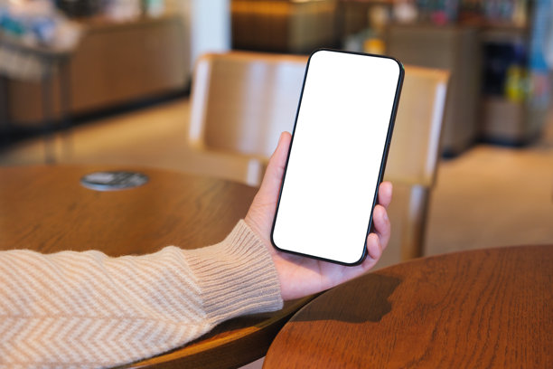 咖啡馆女子手持手机使用，背景为空白桌面屏幕的样机图图片下载