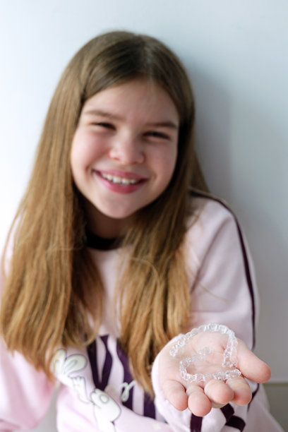 小女孩手中拿着透明牙齿矫正器，展示了儿童现代正畸护理。这是一张适合牙科诊所、牙齿矫正器品牌和健康微笑宣传的明亮生活方式照片。图片下载