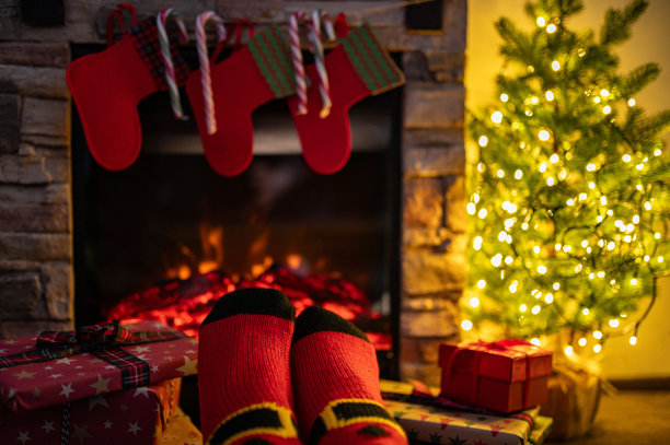 穿着圣诞袜的女性腿部，背景为带有壁炉和深色墙壁的室内装饰。留有足够的空间供您装饰。图片下载