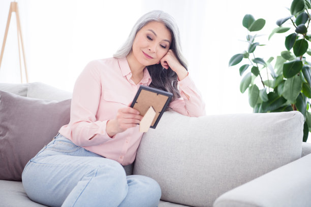 照片：一位长发中年女士穿着粉色衬衫和牛仔裤，独自在家思考的画面图片下载