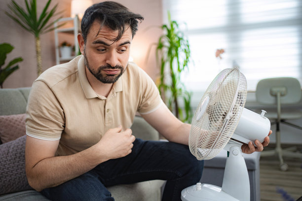 炎热天气在家中，男子用风扇给自己扇风降温图片下载