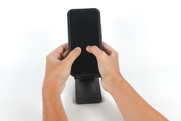 双手握住连接在支架上的手机，用拇指触摸空白屏幕图片下载