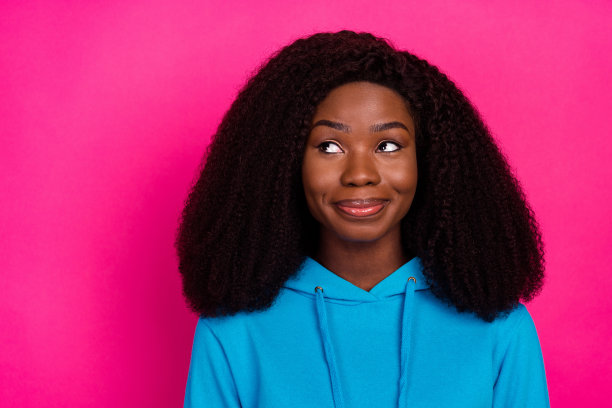 穿着蓝色卫衣的迷人女人，眼神空洞地望向远方，背景是明亮的粉红色，照片肖像图片下载