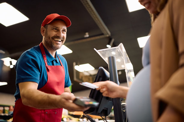 快乐的超市收银员在收银台接受顾客的移动支付。图片下载