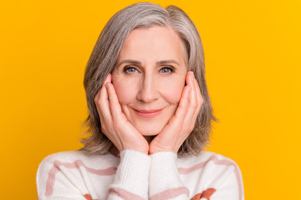 照片：一位戴着毛衣的快乐白发老太太，脸部和手部特写，背景为黄色图片下载