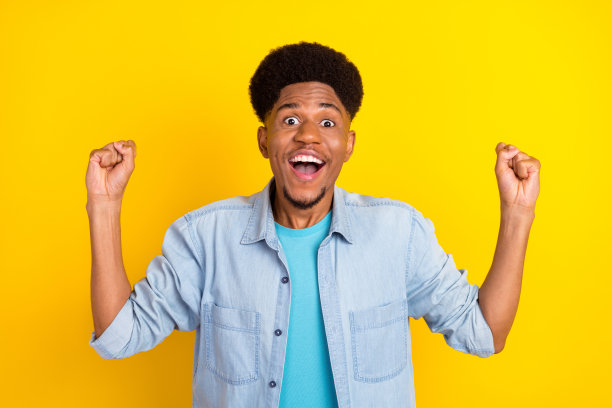 照片：穿着牛仔衬衫、笑容灿烂、举起拳头的时髦黑皮肤男子，在黄色背景前图片下载