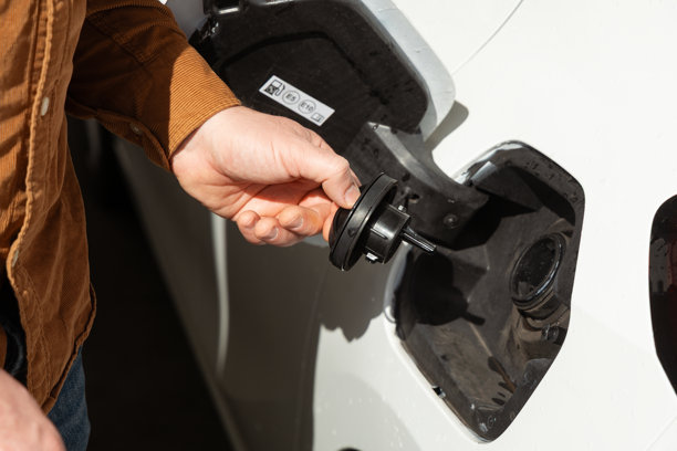 一个人在加油站给汽车加油，手中拿着油枪，汽车近在咫尺图片下载