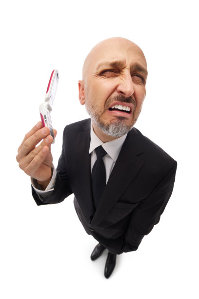 一位身着西装的商人，因接到投诉电话而皱眉表示不满，他手中的翻盖手机。该照片采用广角镜头从上方拍摄，背景为简洁的白色。图片下载