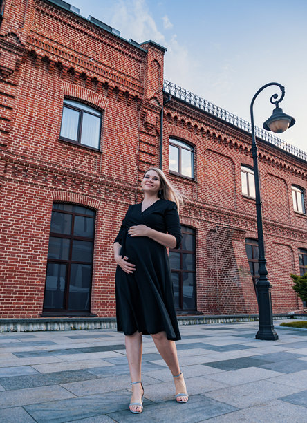 黄昏时分，一位优雅的孕妇身着时尚的黑色连衣裙，在历史悠久的红砖建筑旁摆姿势。图片下载