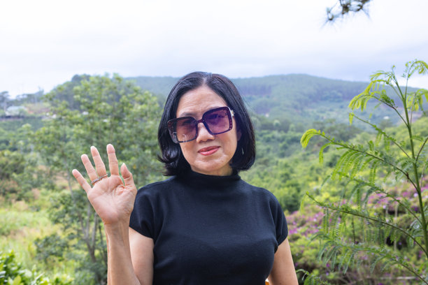 一位女士面带微笑，挥手，直视前方，示意可以打电话、发短信或进行视频通话。摄影素材图片下载